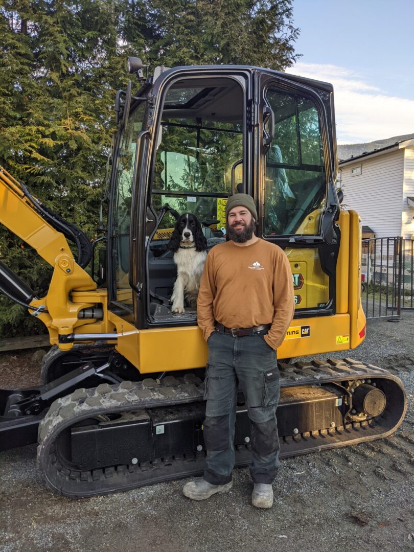 A man and his dog standing in front of a yellow construction vehicle.