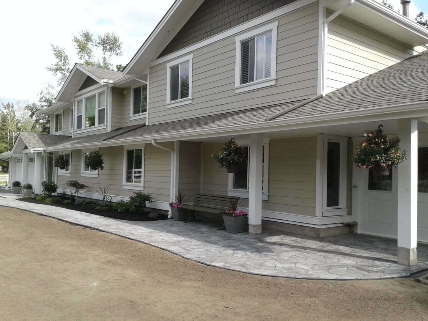 A large two-story home with a beige façade, multiple windows, and a covered porch adorned with hanging flower baskets.