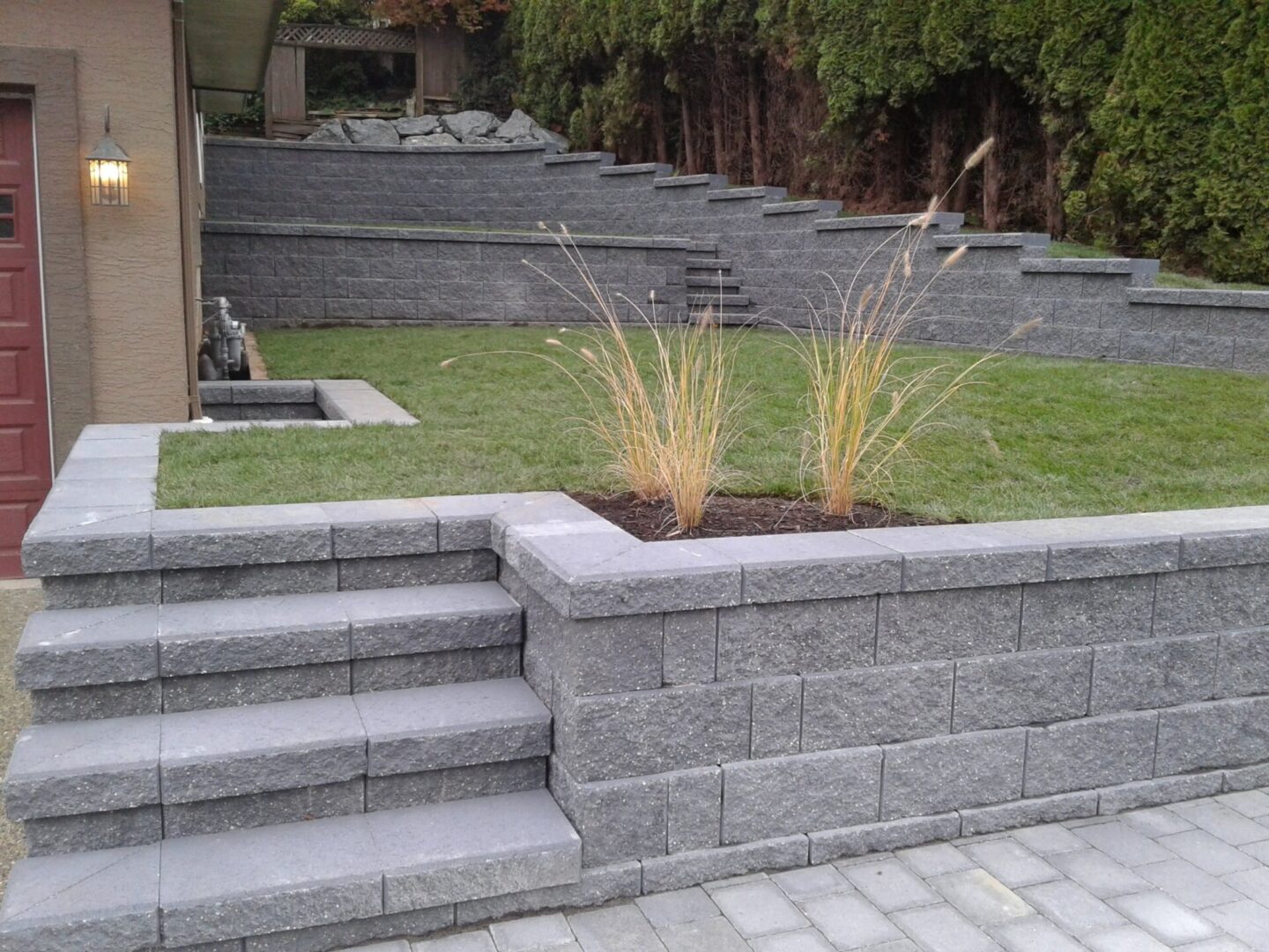 A landscaped backyard with a stone staircase, neatly trimmed grass, ornamental grasses, and layered stone walls.