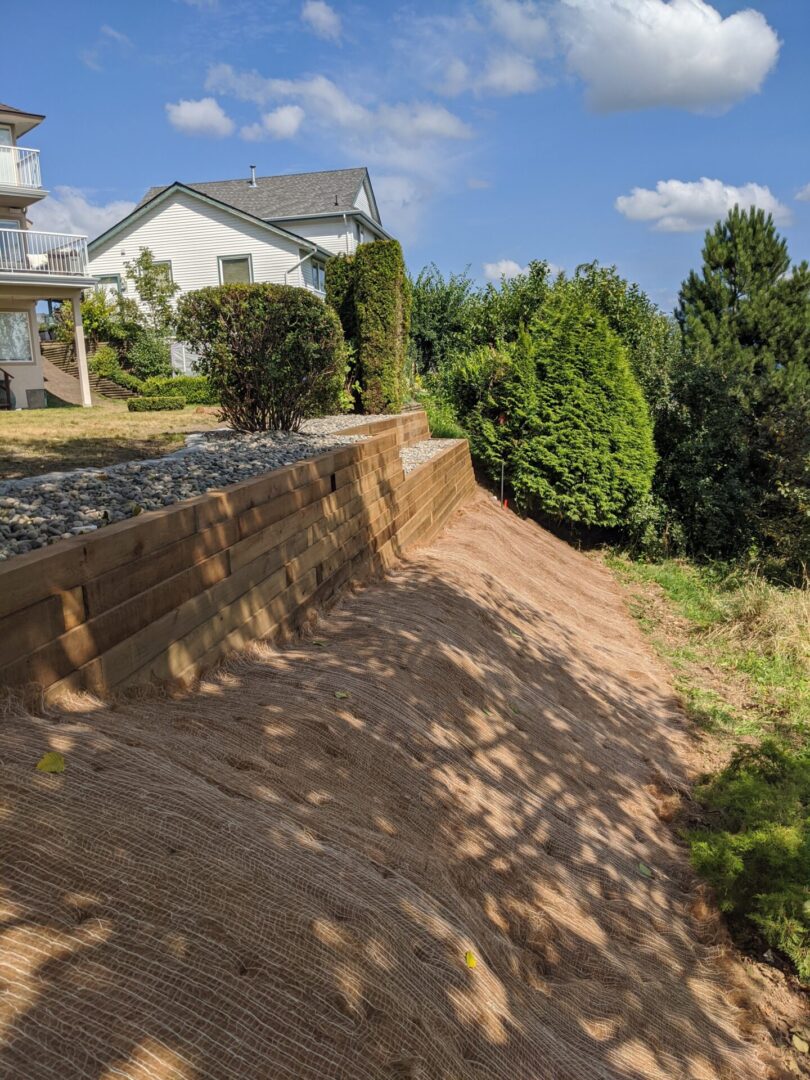 Newly landscaped residential backyard with wooden retaining wall and erosion control netting on a sunny day.