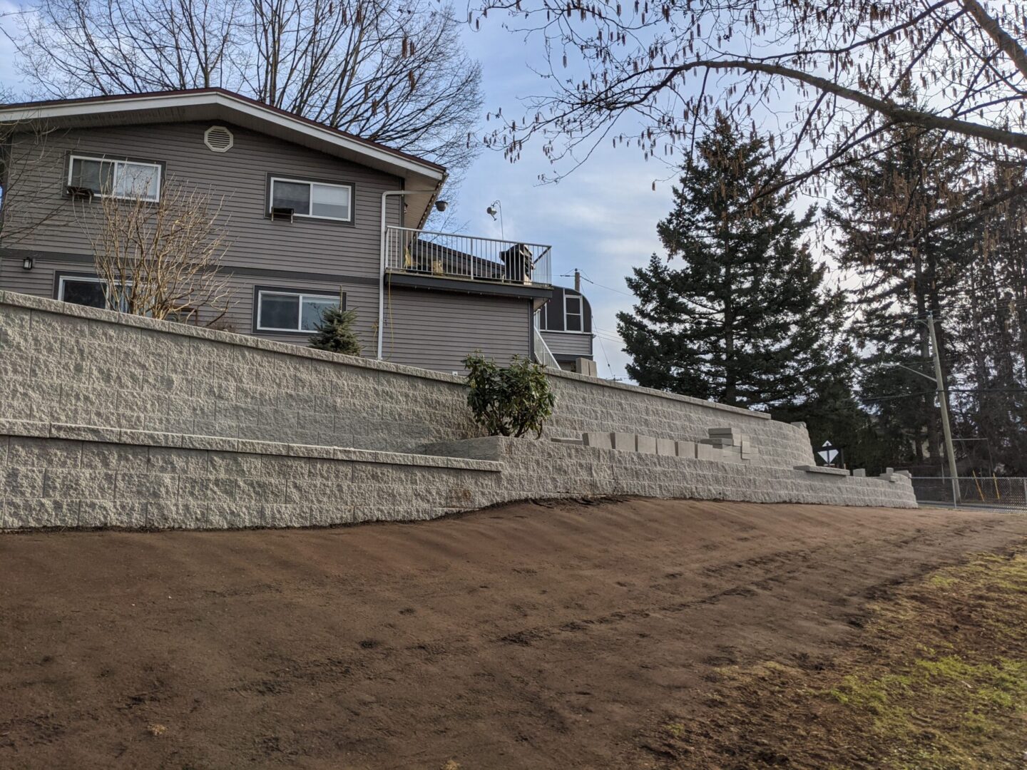 A suburban house with a tall stone retaining wall and a lawn, under a cloudy sky.