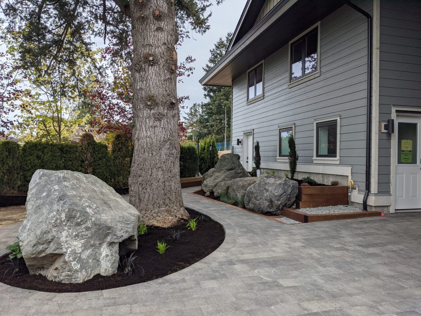 A modern gray house with landscaped front yard featuring large rocks, a tree, and a curved pathway.