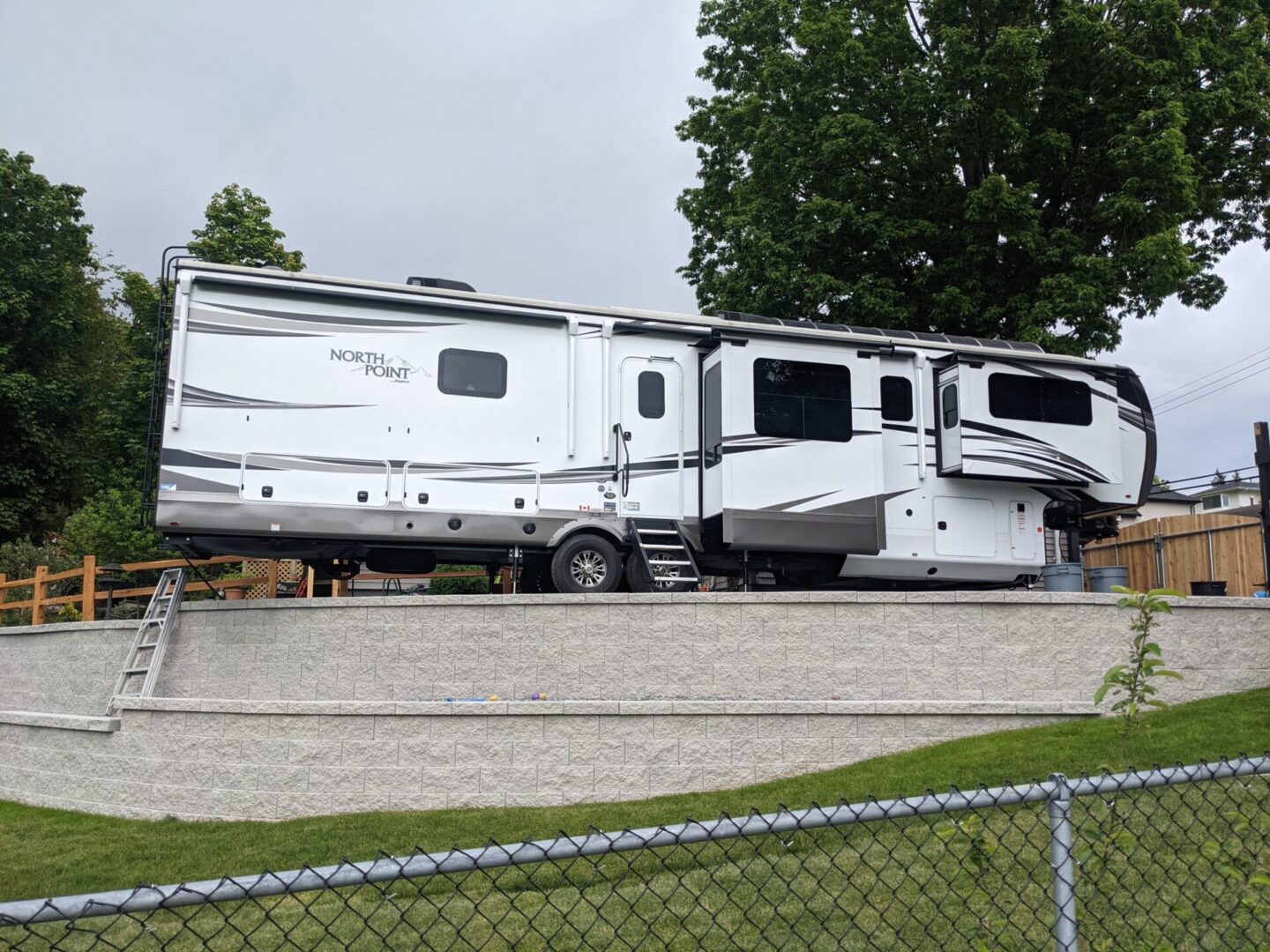 A large, modern north point rv parked on a gravel lot, featuring multiple slide-outs and a small set of stairs leading up to a door.