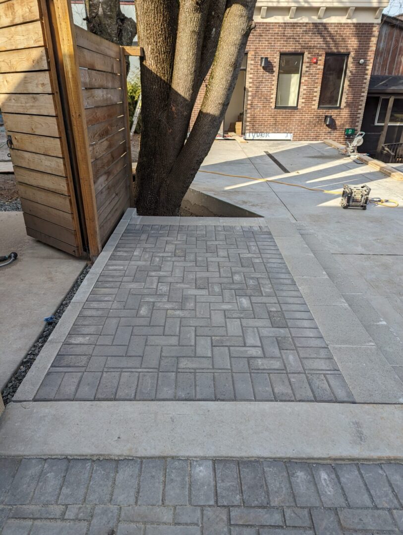 A newly laid herringbone pattern brick pathway leading to a modern house with a large tree nearby.
